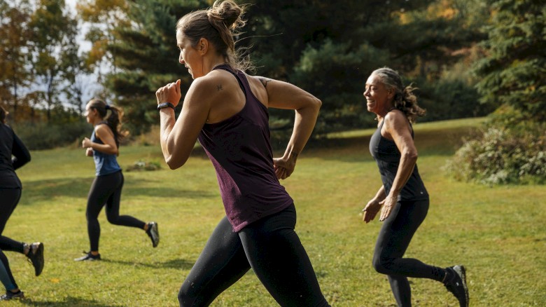 A group of people are running outdoors on a grassy area, surrounded by trees and autumn foliage.