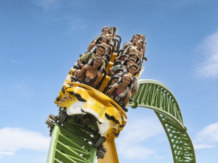 People riding a green and yellow roller coaster on a bright day, appearing thrilled and excited as they experience a thrilling descent.