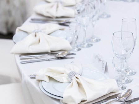 An elegantly set table with white linens, plates, napkins, silverware, and multiple glasses, ready for a formal gathering or event.