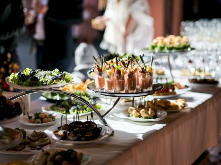 A buffet table with various appetizers and salads arranged on tiered trays, surrounded by glasses ready for guests.