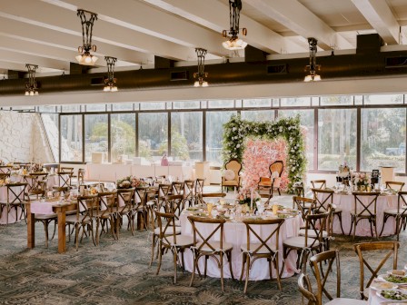 A beautifully decorated banquet hall with round tables, elegant chairs, and floral arrangements, creating a festive atmosphere.