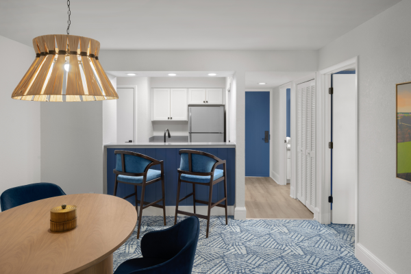 A modern kitchen and dining area with blue and white decor, featuring chairs, a table, pendant light, and blue-patterned carpet.