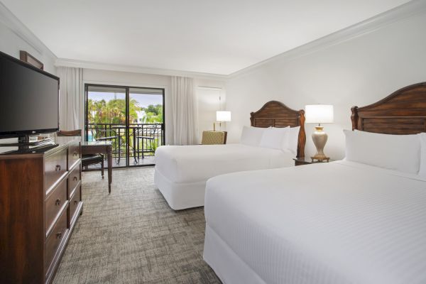 A hotel room with two beds, a TV, desk, and a balcony view.