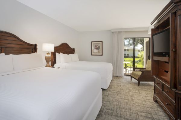 A clean hotel room with two beds, a TV in a cabinet, and a view of the outdoors.