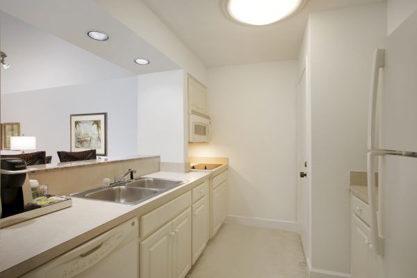 A compact kitchen with white cabinets, sink, microwave, fridge, and a picture on the wall.
