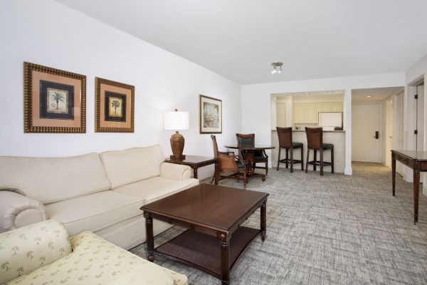 An elegant living room with sofa, chairs, tables, and artwork, leading to a dining area with a table set for four.