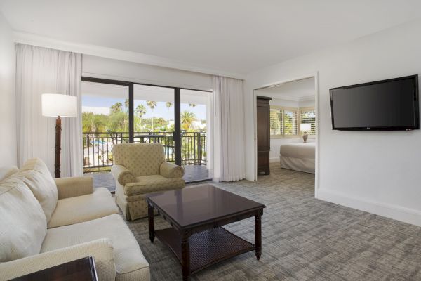 A cozy room with a sofa, chairs, a table, a lamp, a TV, and a view of palm trees.