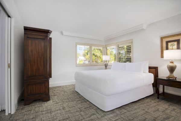 Elegant bedroom with a large bed, wooden furniture, and windows letting in natural light.