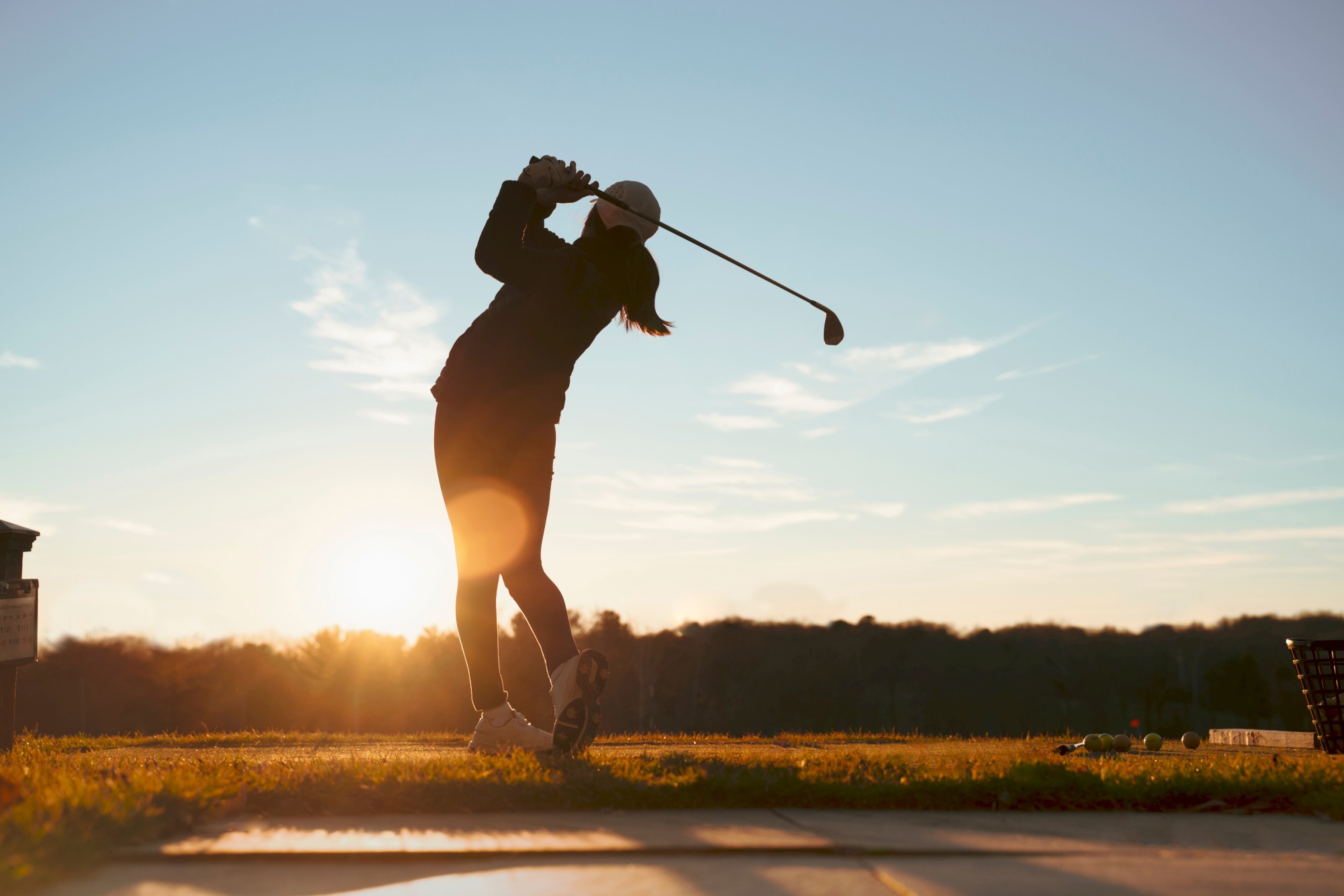 A golfer is captured mid-swing against a sunrise or sunset backdrop on a golf course, highlighting their silhouette.