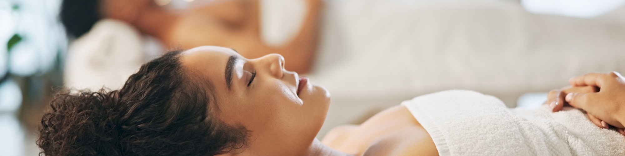 Two people are relaxing in a spa, lying on massage tables with towels, enjoying a peaceful and serene atmosphere.