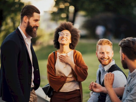 Four people are outdoors, smiling and chatting in a relaxed setting.