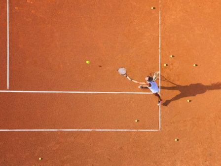 A person on a clay tennis court is preparing to hit a ball, with several tennis balls scattered around.