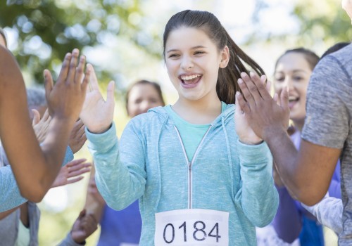 A girl with the number 0184 on her clothes is high-fiving people. She appears happy and is surrounded by others outdoors.