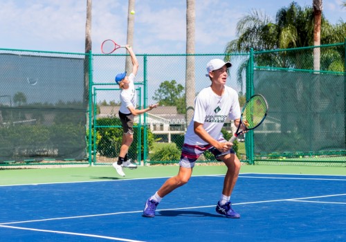 Two people are playing tennis on an outdoor court. One is serving, the other is ready to receive the ball.