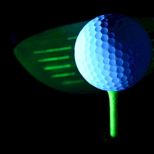 A glowing golf ball on a neon tee in front of a golf club head, set against a dark background.