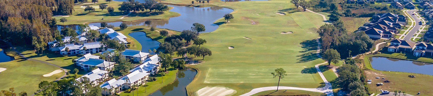 Aerial view of a golf course with water features, surrounded by residential neighborhoods and forested areas.