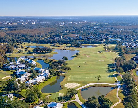 Aerial view of a golf course with water features, surrounded by residential neighborhoods and forested areas.