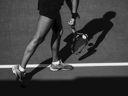 A tennis player on a court with a racket, casting a shadow while hitting the ball.